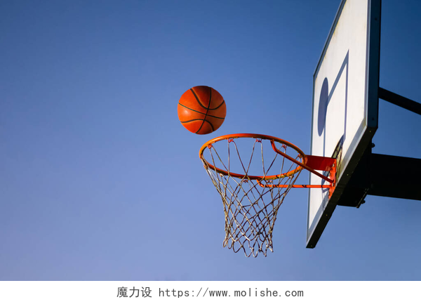 球网上方的篮球街头篮球掉进了篮筐里.在球网上方的橙色球，背景为蓝天。成功的概念,得分和胜利.复制空间